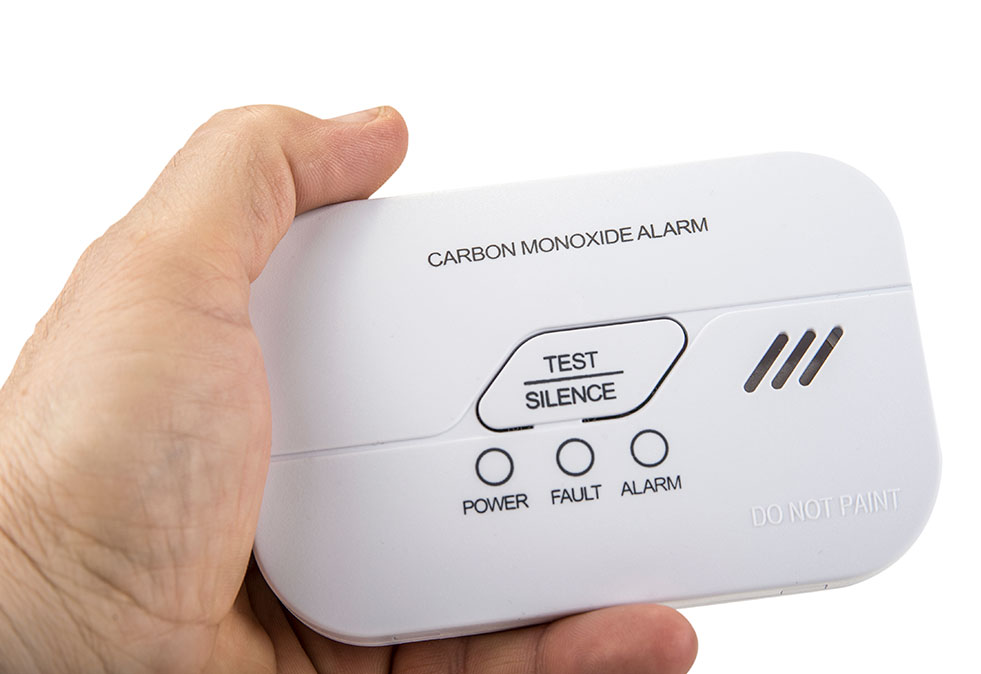 A smoke alarm being held with test, power, fault, and alarm button