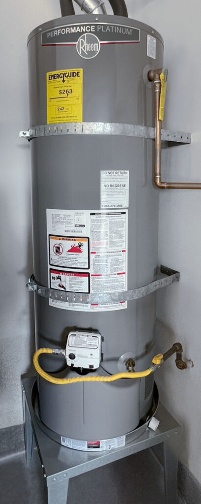 water heater with safety warning labels, Energy Guide label, and earthquake straps on a metal stand.